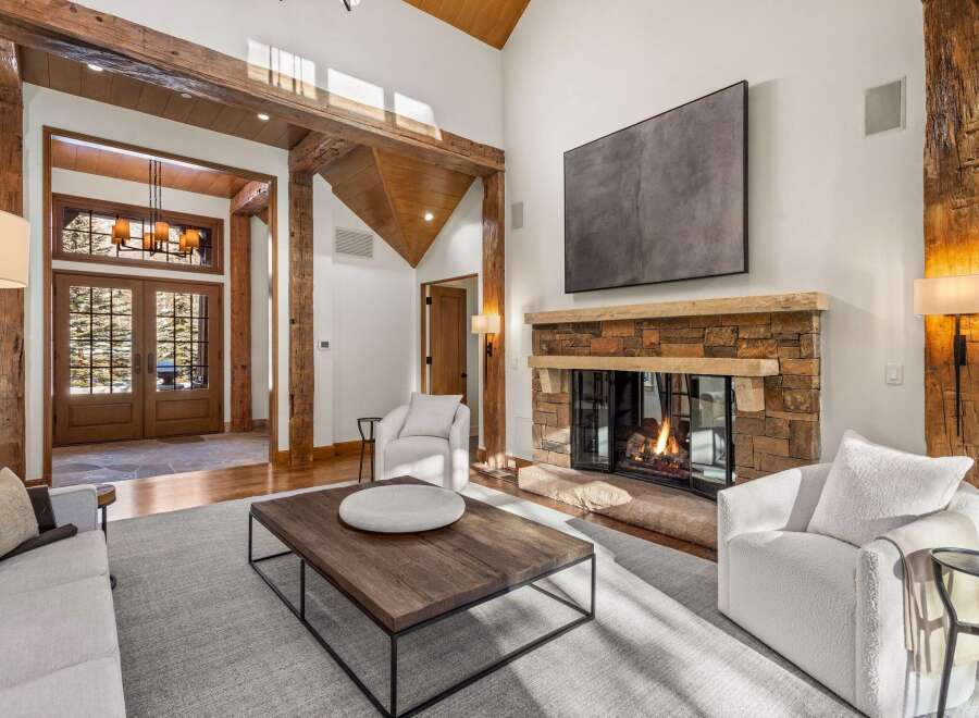 This stunning living room boasts a cozy fireplace, large windows offering natural light, and high ceilings with exposed wooden beams.