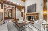 This stunning living room boasts a cozy fireplace, large windows offering natural light, and high ceilings with exposed wooden beams.