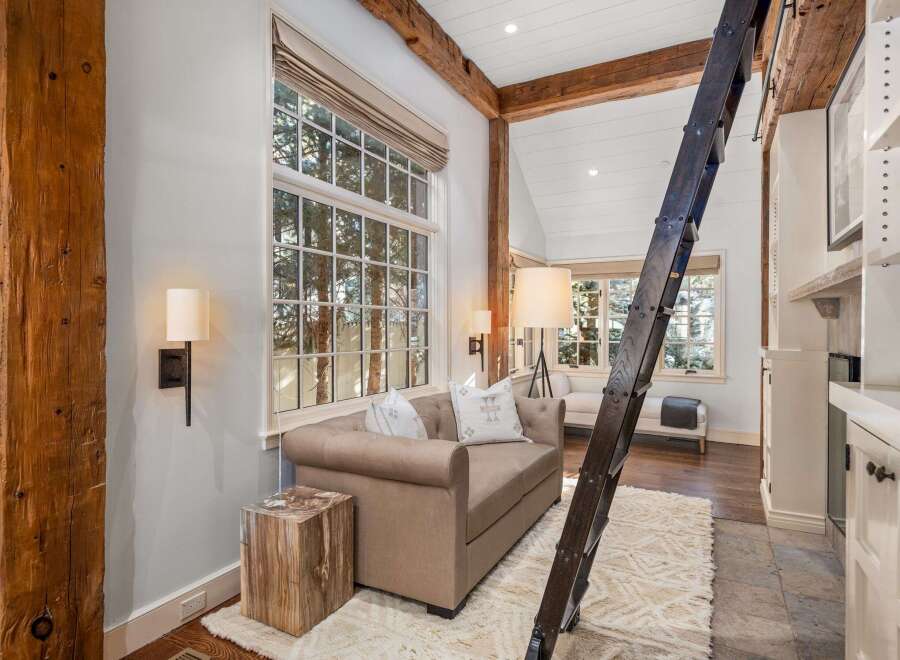 Rustic-chic living space featuring exposed wooden beams, a cozy sofa, and a unique wooden ladder leading to an upper level.