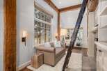 Rustic-chic living space featuring exposed wooden beams, a cozy sofa, and a unique wooden ladder leading to an upper level.