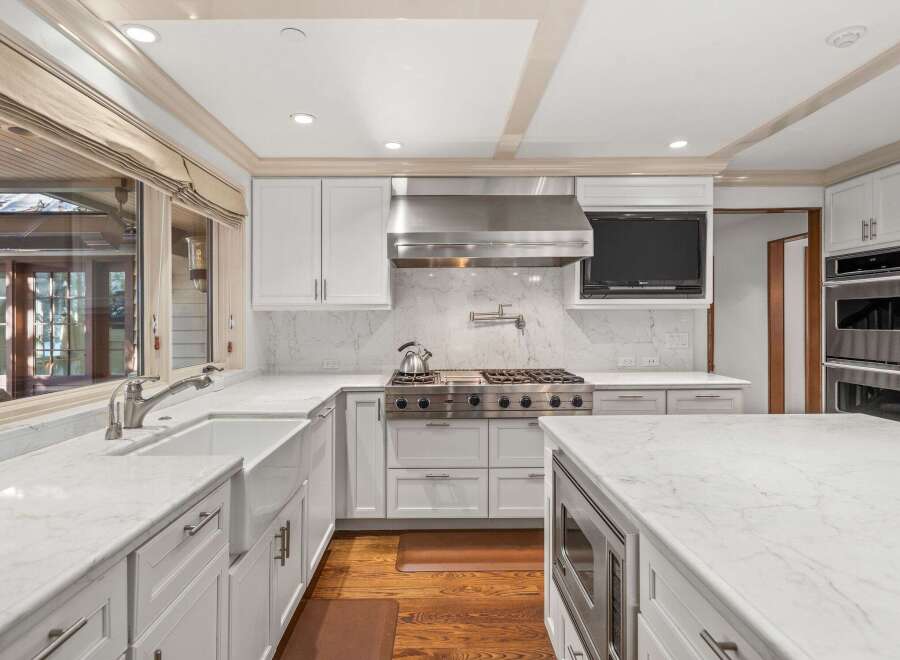 This stunning kitchen boasts a spacious island with built-in microwave, white shaker cabinets, and sleek stainless steel appliances.