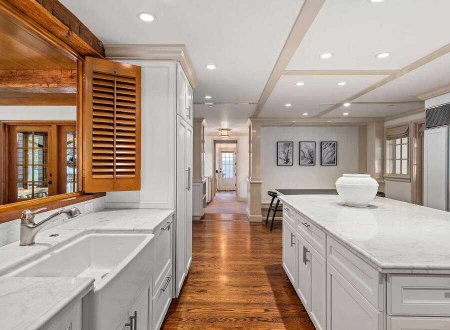 This stunning kitchen boasts a spacious island with marble countertops, white shaker cabinets, and a farmhouse sink.