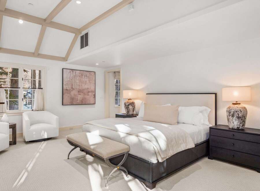 Luxurious bedroom with vaulted ceilings and exposed beams, featuring a plush bed, comfortable seating, and elegant nightstands.