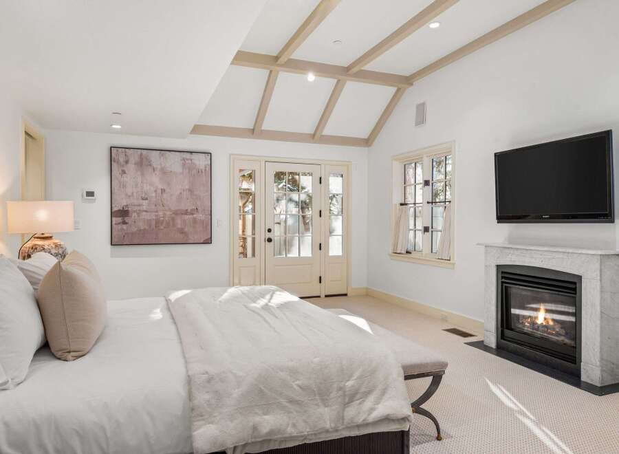 This luxurious bedroom boasts a cozy fireplace, large windows offering ample natural light, and French doors leading to a private outdoor space.