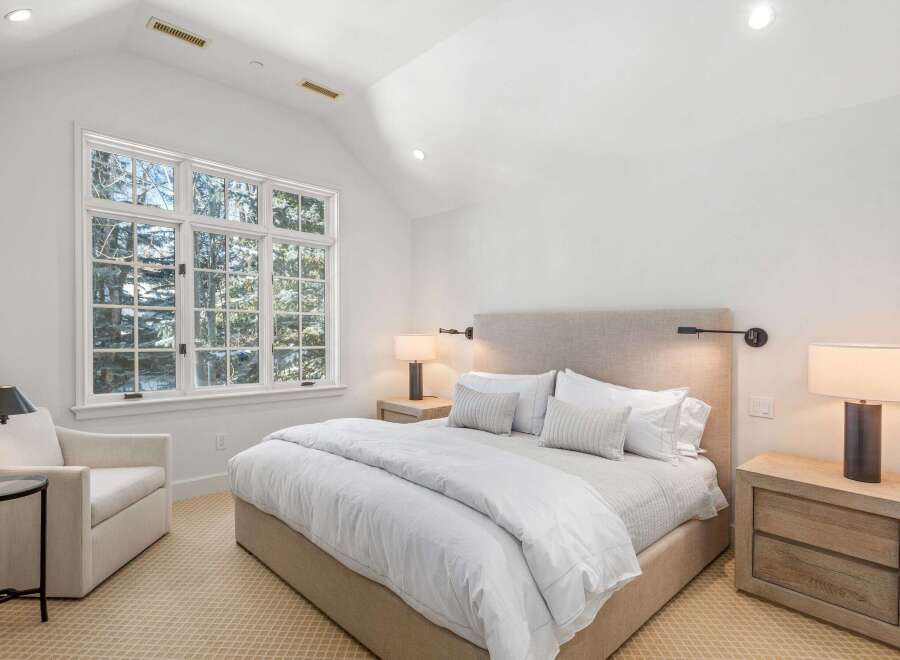 This bright and airy bedroom boasts a cozy atmosphere with its plush bedding, large windows offering scenic views, and stylish nightstands.