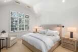 This bright and airy bedroom boasts a cozy atmosphere with its plush bedding, large windows offering scenic views, and stylish nightstands.