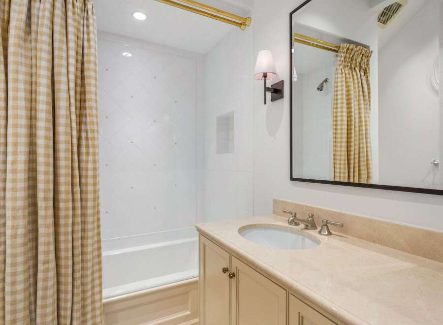 This charming bathroom boasts a classic design with beige gingham shower curtains, white subway tiles, and a beige marble countertop vanity.