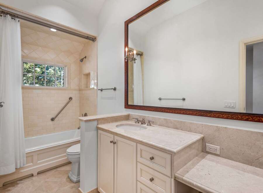 This luxurious bathroom boasts a spacious vanity with marble countertops and ample storage, complemented by elegant off-white cabinets.