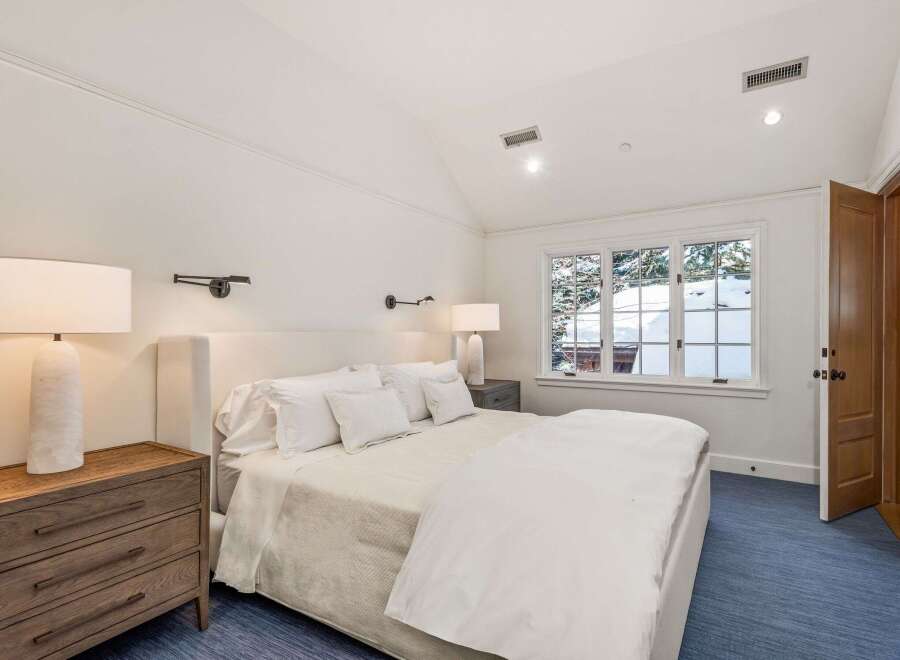 This serene bedroom boasts a king-size bed dressed in crisp white linens, complemented by a plush carpet and soft lighting.