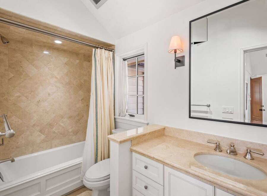 This luxurious bathroom boasts a spacious bathtub, a stylish vanity with marble countertops, and an elegant shower with beige tile.