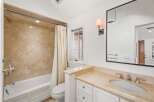 This luxurious bathroom boasts a spacious bathtub, a stylish vanity with marble countertops, and an elegant shower with beige tile.