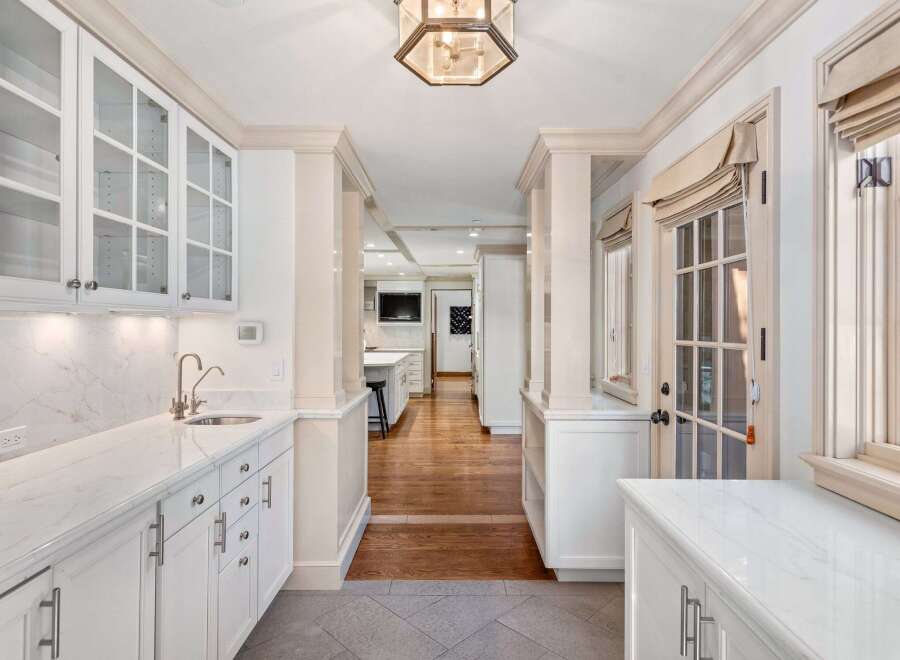 This stunning kitchen boasts a spacious design with white cabinetry, glass-front upper cabinets, and sleek marble countertops.