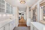This stunning kitchen boasts a spacious design with white cabinetry, glass-front upper cabinets, and sleek marble countertops.