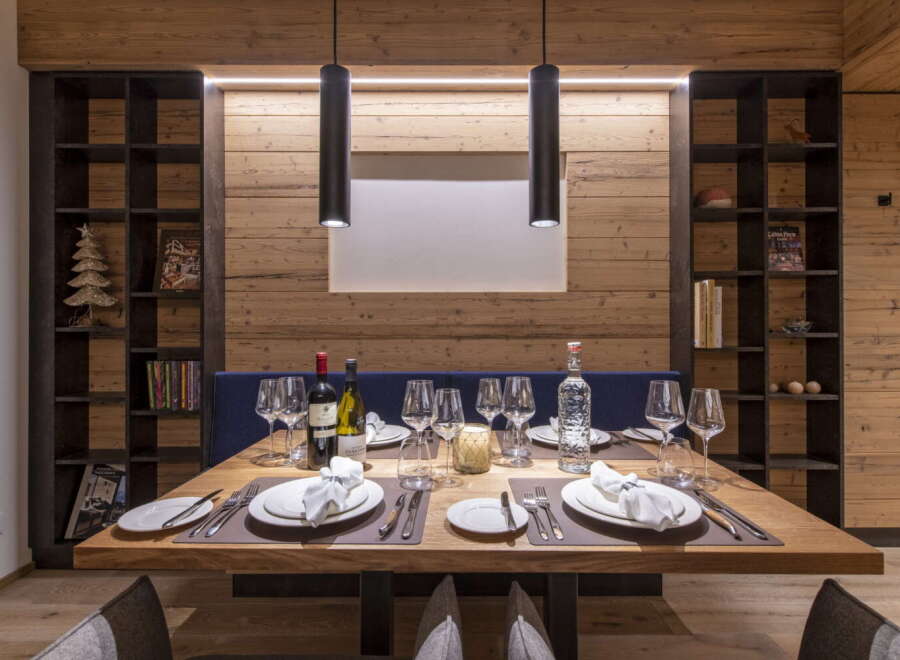 This stunning dining area features a rustic wooden wall, complemented by sleek black pendant lights and modern shelving units.