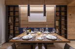This stunning dining area features a rustic wooden wall, complemented by sleek black pendant lights and modern shelving units.