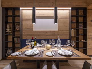 This stunning dining area features a rustic wooden wall, complemented by sleek black pendant lights and modern shelving units.