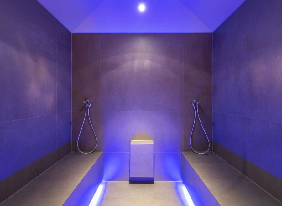 This luxurious spa features a stunning steam room with sleek, dark gray tile and ambient purple lighting.