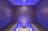 This luxurious spa features a stunning steam room with sleek, dark gray tile and ambient purple lighting.