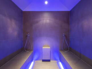 This luxurious spa features a stunning steam room with sleek, dark gray tile and ambient purple lighting.