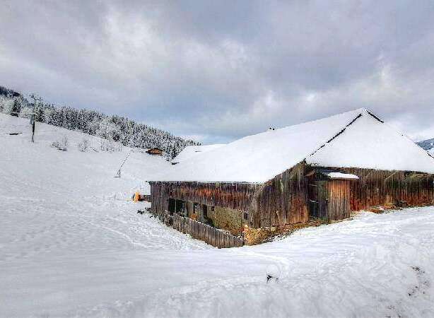 Discover this charming rustic barn nestled in a breathtaking snowy mountain landscape.