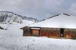 Rustic wooden barn nestled in a snowy mountain landscape.