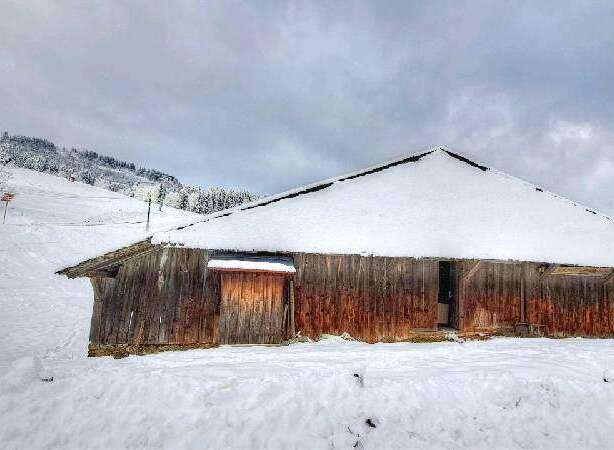 Rustic wooden barn nestled in a snowy mountainside, offering a serene escape.