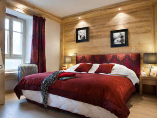 Cozy chalet bedroom with wooden walls, a plush red duvet, and tasteful decor.