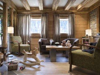 This stunning chalet boasts a spacious living area with large windows offering breathtaking views, hardwood floors, and comfortable armchairs perfect for relaxing.