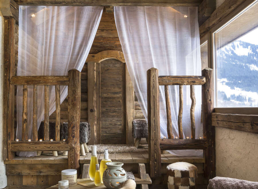 Nestled in a rustic wooden cabin, this luxurious spa boasts a tranquil treatment room with sheer curtains and soft lighting.