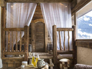Nestled in a rustic wooden cabin, this luxurious spa boasts a tranquil treatment room with sheer curtains and soft lighting.