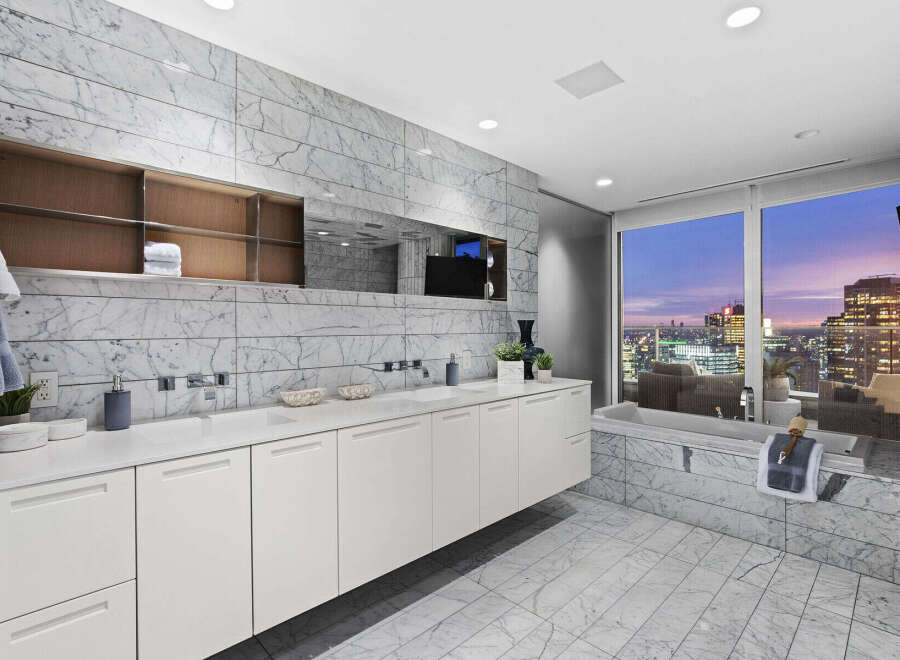 Luxury bathroom with city views features marble flooring and walls, a floating vanity with white cabinets, and a soaking tub.