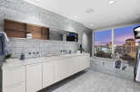 Luxury bathroom with city views features marble flooring and walls, a floating vanity with white cabinets, and a soaking tub.