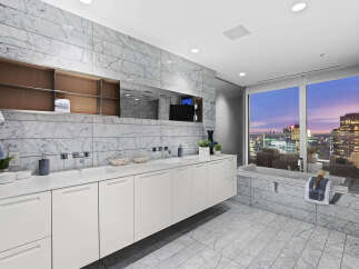 Luxury bathroom with city views features marble flooring and walls, a floating vanity with white cabinets, and a soaking tub.
