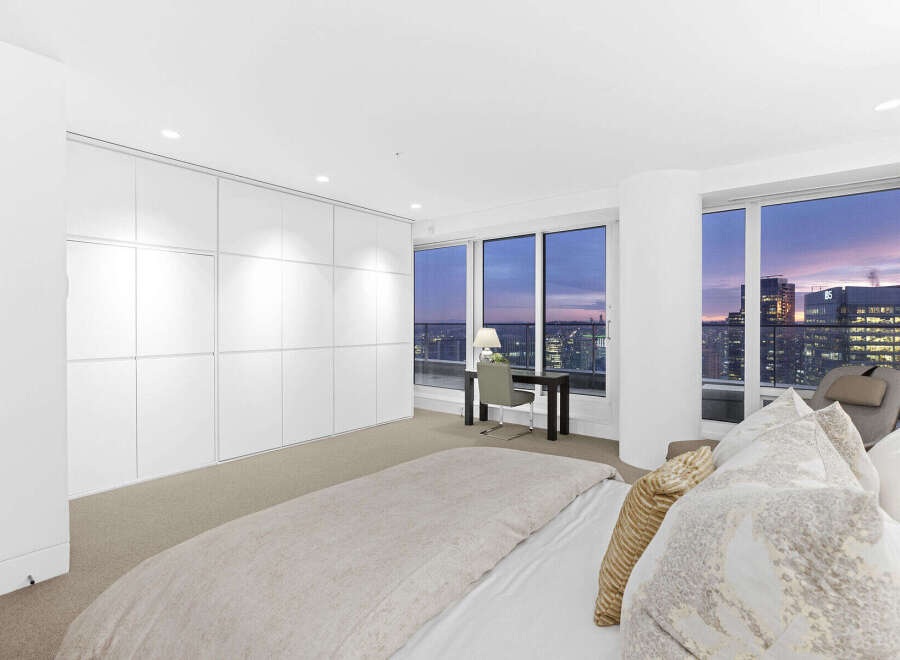 Luxurious penthouse bedroom boasts floor-to-ceiling windows showcasing breathtaking city skyline views.