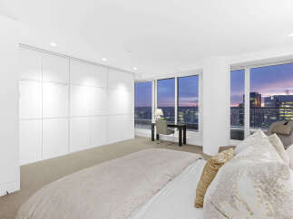 Luxurious penthouse bedroom boasts floor-to-ceiling windows showcasing breathtaking city skyline views.