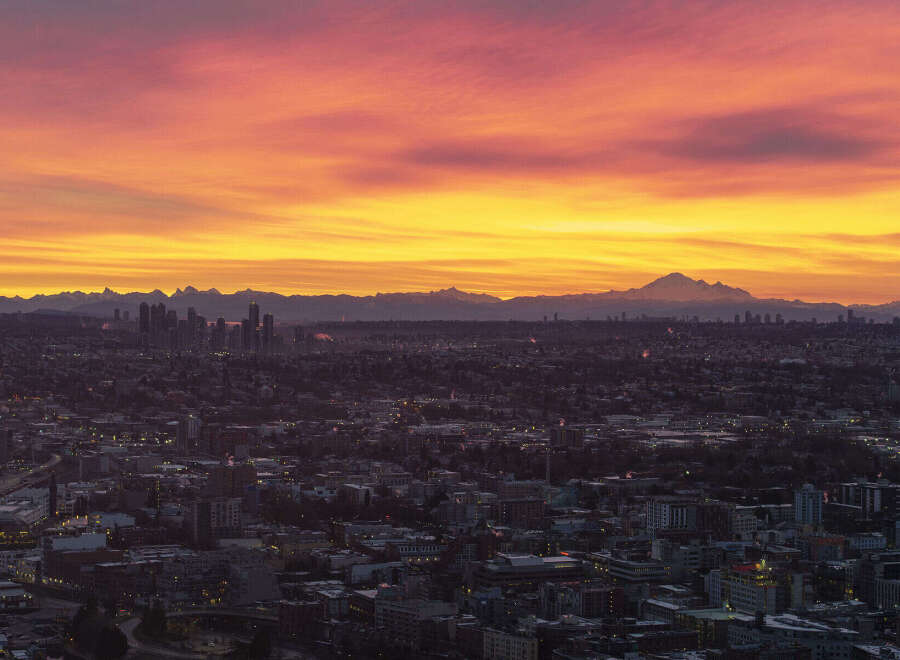 Spectacular sunrise over a sprawling cityscape, with a majestic mountain range in the distance.