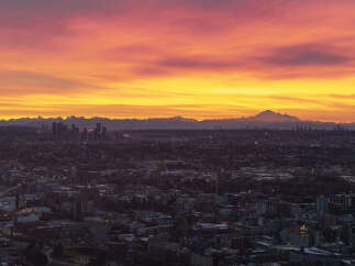 Spectacular sunrise over a sprawling cityscape, with a majestic mountain range in the distance.