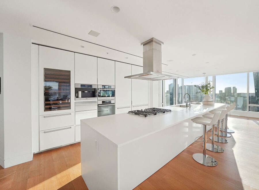 This luxurious kitchen boasts sleek white cabinetry, top-of-the-line stainless steel appliances, and a spacious island with seating.