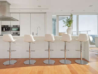 Modern kitchen with white cabinetry and stainless steel appliances, featuring a breakfast bar with four sleek white bar stools.