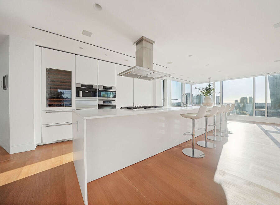 This luxurious kitchen boasts sleek white cabinetry, high-end stainless steel appliances, and a large island with seating, perfect for entertaining.