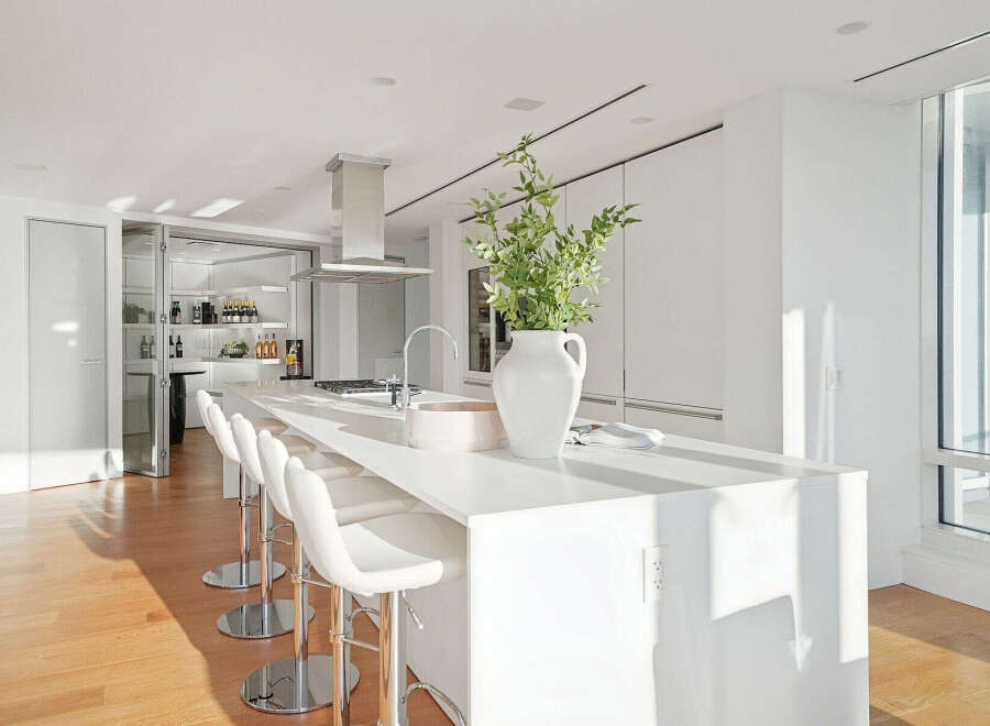 This stunning kitchen boasts a sleek, modern design with white cabinetry and countertops, complemented by a large island with seating.