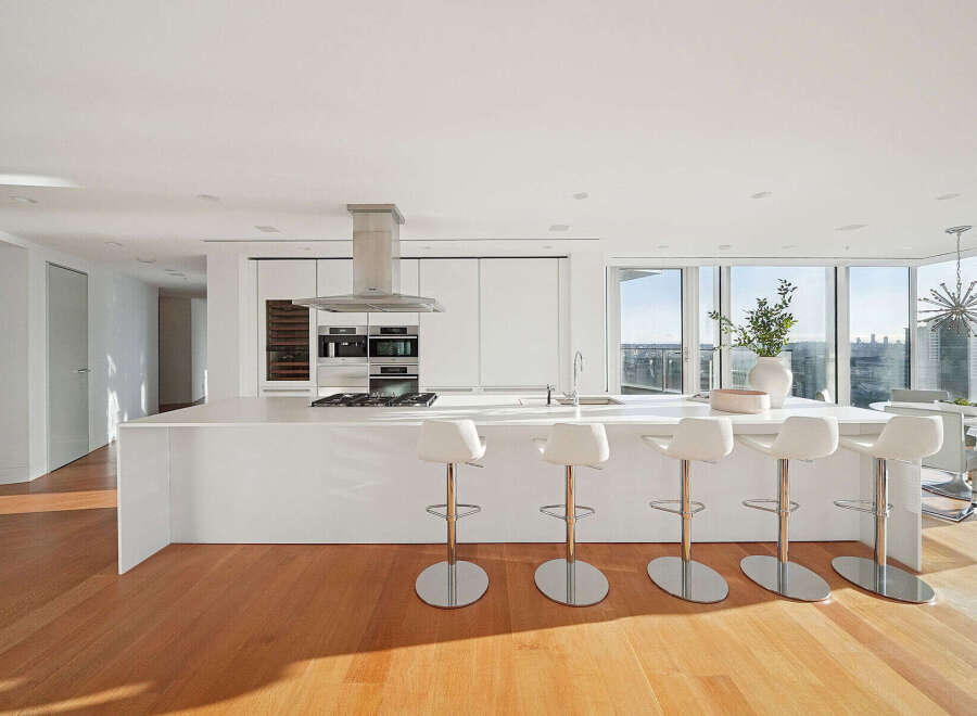 This luxurious condo boasts a stunning modern kitchen with sleek white cabinetry, high-end stainless steel appliances, and a large island with seating.