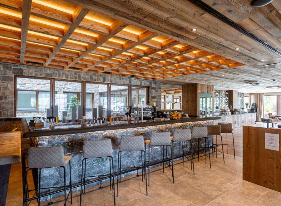 Discover a cozy bar area, designed with a unique stone bar, comfortable stools, and a warm, inviting wooden ceiling with integrated lighting.