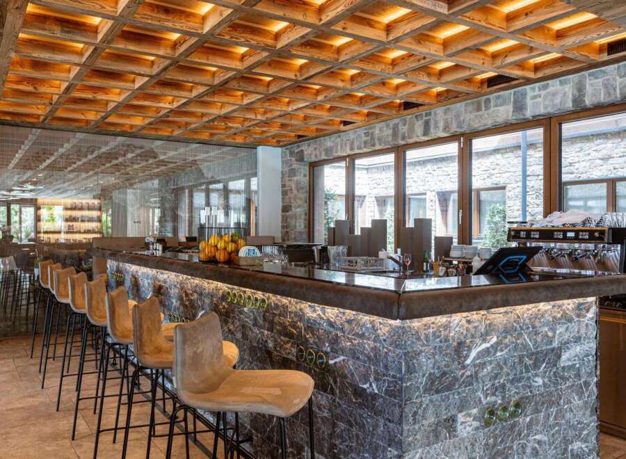 This stylish bar area features a unique wooden grid ceiling with warm lighting, complemented by marble countertops and stone walls.