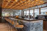 This stylish bar area features a unique wooden grid ceiling with warm lighting, complemented by marble countertops and stone walls.