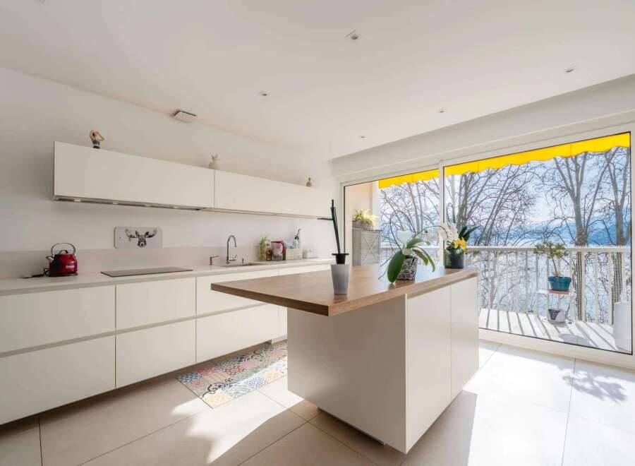 Modern kitchen with white cabinets and wooden island, offering stunning lake views through large windows.