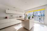 Modern kitchen with white cabinets and wooden island, offering stunning lake views through large windows.