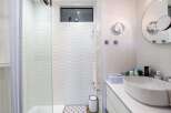This stunning bathroom boasts a modern design with white wave-patterned tiles, a sleek glass shower enclosure, and a stylish oval sink.