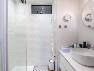 This stunning bathroom boasts a modern design with white wave-patterned tiles, a sleek glass shower enclosure, and a stylish oval sink.