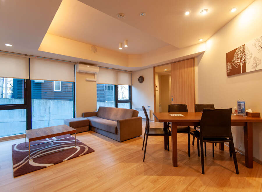 This modern apartment boasts an open-plan living area with hardwood floors, large windows offering ample natural light, and a comfortable sofa set.